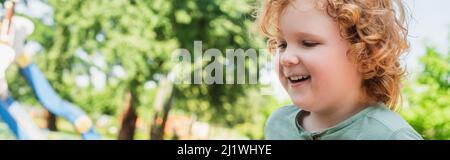 Porträt eines Rotkopfjungen mit lockigen Haaren, lächelnd im Freien, Banner Stockfoto