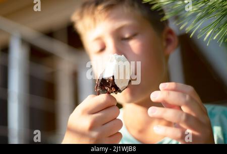 Der Junge isst Schokoladeneis. Unschärfes Gesicht. Eskimo auf einem Stock in der Hitze. Stockfoto