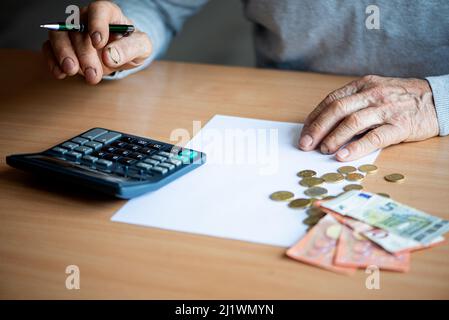 Hände eines alten älteren Mannes mit Rechner und Rechnungen, die zu Hause Euro-Geld zählen. Stockfoto