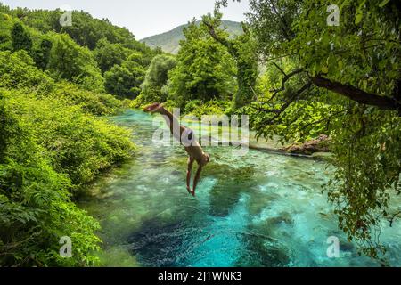 Nicht identifizierter Mann springt in die wunderschöne türkisfarbene Quelle Blue Eye oder Syri i Kalter in der Nähe der Stadt Muzine in Albanien. Stockfoto