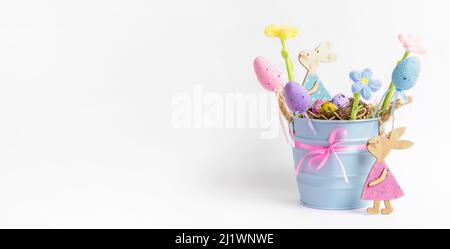 Interieur Kinder Urlaub Komposition mit kleinen blauen Eimer mit Nest von farbigen Wachteleiern, dekorative Eier, gestrickte Farbblumen, Holzhasen o Stockfoto
