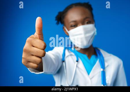 Portrait glückliche afroamerikanische Ärztin mit OK-Zeichen im blauen Studio Stockfoto
