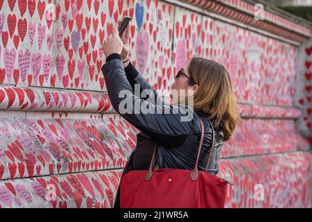 LONDON, GROSSBRITANNIEN. 28 März, 2022 . Ein Mitglied der Öffentlichkeit hält ein Mobiltelefon, um die gemalten Herzen an der nationalen Gedenkmauer zu fotografieren, um an die Opfer der Coronavirus-Pandemie zu erinnern. Die Zahl der Fälle ist nach Angaben des britischen Statistikamts durch das Omicron BA gestiegen.2 Variante ein rekombinantes Virus, das Elemente der Delta- und Omicro-Varianten enthält, da die Zahl der COVID-19-Infektionen in den sieben Fällen auf 4,26 Millionen stieg Tage bis zum 19. März - Anstieg um 29,7% gegenüber der Vorwoche. Kredit: amer ghazzal/Alamy Live Nachrichten Stockfoto