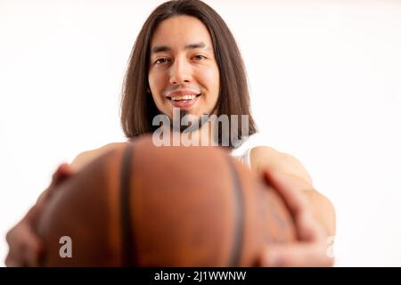 Porträt eines lächelnden kaukasischen langhaarigen bärtigen Mannes, der den Basketballball vor die Kamera hält. Fokussieren Sie auf Aufnahmen aus der Mitteldistanz auf weißem Hintergrund. Hochwertige Fotos Stockfoto