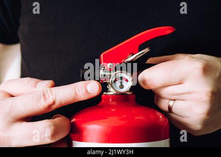 Nahaufnahme eines Mitarbeiters, der den roten Feuerlöscher zeigt und ihn kontrolliert. Wartungsdienstkonzept. Stockfoto