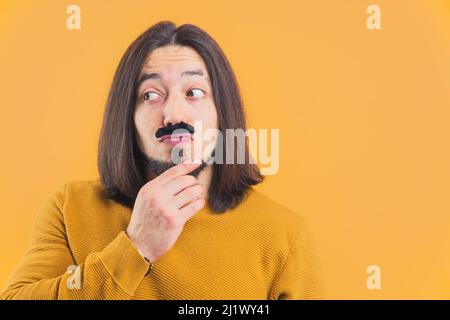 Movember-Konzept. Lustiger kaukasischer Mann, der dumme Gesichter macht, während er gefälschten Schnurrbart trägt. Hochwertige Fotos Stockfoto