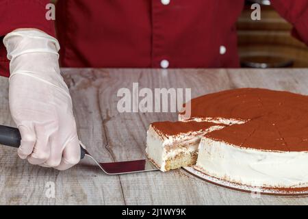 Tiramisu Kuchen mit einem Schnitt mit einer Scheibe und einer Klinge auf einem grauen Hintergrund, Nahaufnahme Stockfoto