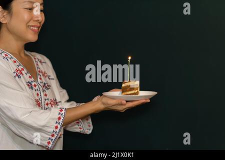 Frau Hand hält ein Stück Geburtstagskuchen auf dem Teller mit Kerze. Stockfoto