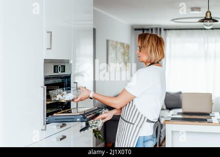 Gebackener Lachs mit grünem Spargel – Rezeptschritte. Schritt 5. Frau, die Backform mit Fisch und Gemüse in den Ofen legt. Schritt für Schritt Rezept. Gesund Stockfoto