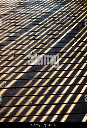 Schatten auf Holzsteg mit Holzgeländer bilden diagonale Boxen Stockfoto