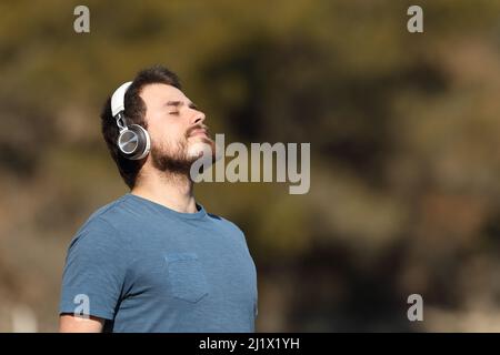 Mann mit kabellosen Kopfhörern, der in der Natur meditierend und hörend meditiert Stockfoto