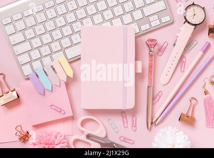 Hardcover-Notizbuch, rosa Schulzubehör und Tastatur auf hellrosa, Draufsicht, Textbuch-Modell. Girly Arbeitsplatz mit Notizbuch, Schere, Bleistift, pe Stockfoto