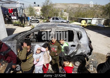 Nablus, Palästina. 28. März 2022. Palästinensische Kinder stehen neben einem verbrannten Auto, nachdem israelische Siedler vier palästinensische Autos angezündet, ihr Eigentum zerstört und ihre Häuser im Dorf Jalud südlich von Nablus im besetzten Westjordanland zerstört haben. Viele der israelischen Siedler randalierten in den palästinensischen Dörfern in der Nähe der Außenposten nach einem Schussangriff von Palästinensern im besetzten Hadera-Gebiet im Jahr 1948. Kredit: SOPA Images Limited/Alamy Live Nachrichten Stockfoto