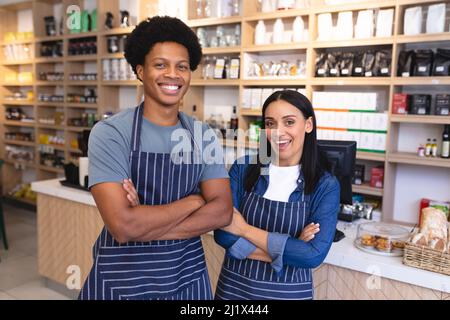 Porträt von glücklichen biracial Coffee Shop Mitarbeiter stehen mit Armen gekreuzt tragen Schürzen. Unverändert, Café-Kultur, Menschen und Beruf Konzept. Stockfoto