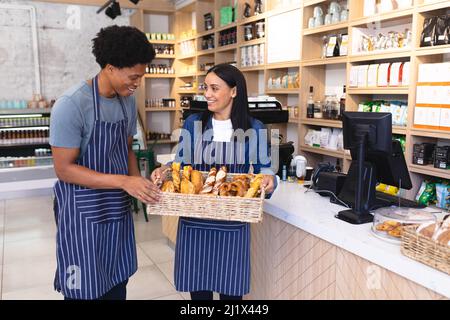 Lächelnde junge, multirassische Mitarbeiter diskutieren über Brezeln im Korb im Café. Unverändert, Café-Kultur, Menschen und Beruf Konzept. Stockfoto