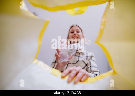 Bild aus dem Inneren gelbe Recycling-Tasche von Frau werfen eine Plastikflasche zu recyceln. Stockfoto