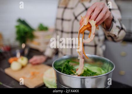 Frau wirft Gemüseschnitzel in einen Komposteimer in der Küche. Stockfoto