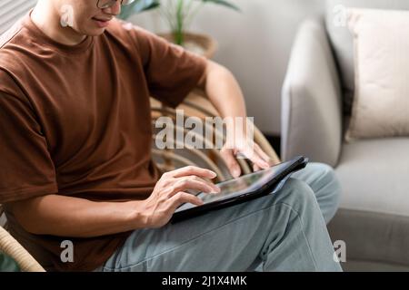 Technologiekonzept der Mann mit seinem lässigen T-Shirt und Jeans sitzt bequem auf dem Holzstuhl und macht einen Touchscreen, um die Webbrowsen zu überprüfen Stockfoto