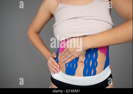 Die junge Frau zeigt Kinesio-Bänder auf ihrem Körper. Kinesio Taping, Verstauchungen, Verletzungen und Muskelschmerzen Konzept Stockfoto