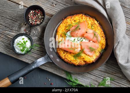 Großer knuspriger Kartoffelpfannkuchen mit geräuchertem Lachs und saurer Creme mit frischen grünen Kräutern, serviert in einer eisernen Pfanne Stockfoto