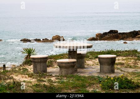 Steintisch und Bänke mit Meerblick, romantische Szenen am Meer. Blick auf die Sandklippen am Strand auf das Meer. Essen mit Meerblick. Steintisch. Stockfoto