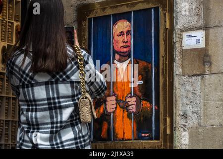 Barcelona, Spanien. 28. März 2022. Ein Pendler fotografiert ein Graffiti des italienischen Stadtkünstlers „TVBoy“, Salvatore Benintende, mit dem Titel „der Traum“, auf dem der russische Präsident Wladimir Putin aus Protest gegen die anhaltenden russischen Angriffe im Gefängnis und hinter Gittern abgebildet ist.Quelle: Matthias Oesterle/Alamy Live News Stockfoto