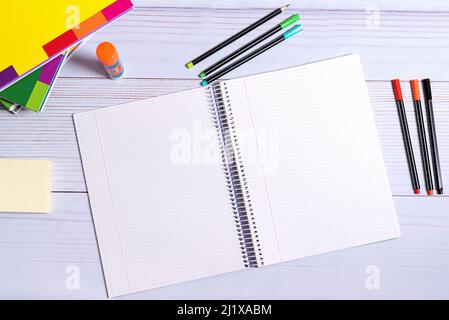 SCHULBEDARF. BUCH GEKIPPT UND GEÖFFNET. NOTIZBUCH, FARBIGE STIFTE. GESTAPELTE BÜCHER UND GLOBUS. Stockfoto