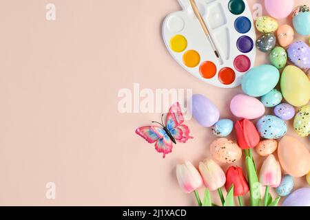 Osterhintergrund mit bemalten Eiern, Tulpen, Farben und Schmetterlingen auf beige. Stockfoto