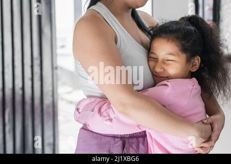 Schönes und zartes Mädchen mit brauner Haut (Latina) umarmt ihre Mutter mit einem glücklichen Gesicht. Tochter umarmt ihre Mutter fest, während sie ihre Augen schließt. Mädchen Stockfoto