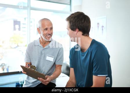 Eine vollständige Aufzeichnung der Gesundheit seiner Patienten. Abgeschnittene Aufnahme eines hübschen reifen männlichen Physiotherapeuten, der eine Konsultation mit einem Patienten hat. Stockfoto