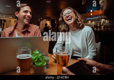 Eine vielfältige Gruppe von Kollegen, die an einem Laptop und einem digitalen Gerät für Getränke arbeiten Stockfoto