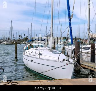 Weißes Segelboot mit Mast und Takelage wird mit Seilen am Dock in einer Marina befestigt. Stockfoto