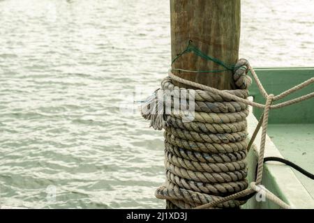 An einem Holzpfahl auf einem Bootssteg befestiges nautisches Seil mit Wasser im Hintergrund. Stockfoto