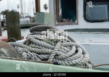 Seil stapelte sich an Deck eines alten Fischerbootes in der Marina, in Nahaufnahme mit begrenztem Fokus und geringer Schärfentiefe. Stockfoto