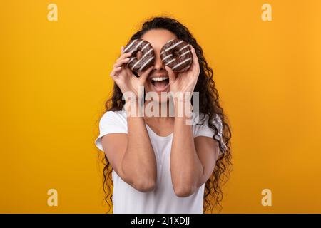 Lustige Dame, Die Im Studio Die Augen Mit Donuts Bedeckt Stockfoto