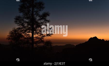 Atemberaubende Aussicht über die Berge der Insel Gran Canaria, Kanarische Inseln, Spanien nach Sonnenuntergang mit bunten dramatischen Himmel und die Silhouetten von Bäumen. Stockfoto