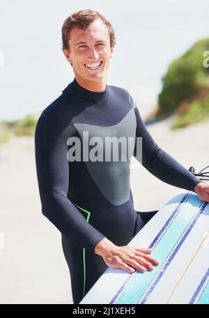 Bereit, die Wellen zu schlagen. Ein Surfer, der sein Board auf seinem Bein ruht und sich für eine Surf-Session vorbereitet. Stockfoto