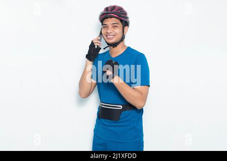 Junger hübscher asiatischer Mann mit Fahrradhelm und Mobiltelefon auf weißem Hintergrund isoliert Stockfoto