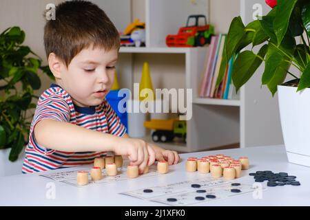 Ein 4-jähriger Junge spielt loto und studiert Zahlen anhand eines Brettspiels. Stockfoto