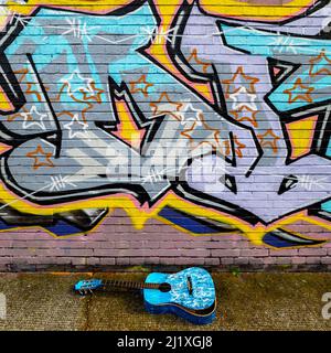 Graue Eagle Street Graffiti mit gebrochener blauer Gitarre im Vordergrund. Spitalfields in London. Stockfoto