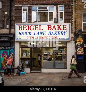 Obdachloser kaukasischer Mann, der auf dem Bürgersteig vor einer Backstube in der Brick Lane sitzt und von zwei weiblichen Passanten Geld erhalten hat. London. VEREINIGTES KÖNIGREICH Stockfoto