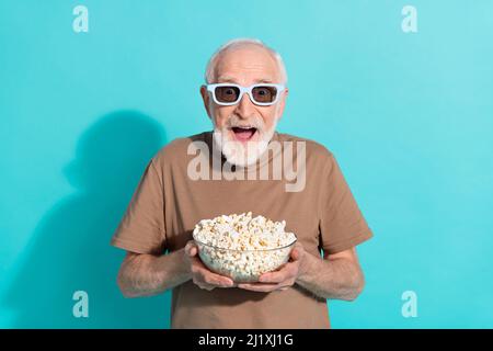 Portrait von attraktiven erstaunt fröhlich grauhaarigen Mann essen Popcorn Spaß isoliert über glänzendes blaues Hintergrund Stockfoto