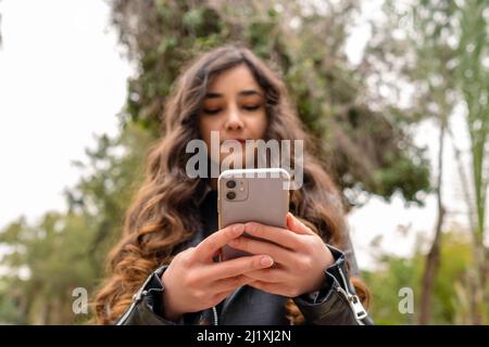 Schöne Frau, die auf dem Handy herumstöbert, während sie auf der Stadt steht. Erfolgreiche Geschäftsfrau überprüft E-Mails während einer Mittagspause draußen auf dem Smartphone. Stockfoto