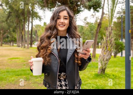 Selbstbewusst glücklich schöne junge Geschäftsfrau Blick auf die Kamera mit einer Tasse Kaffee und Telefon. Sie ist sehr glücklich. Positive hübsche Frau lächelt an der Kamera Stockfoto