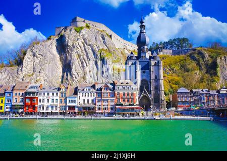 Dinant, Belgien - März 9. 2022: Blick über den Fluss maas auf eine malerische Reihe von alten bunten Häusern, Felswand mit Zitadelle, gotische Kirche gegen cle Stockfoto