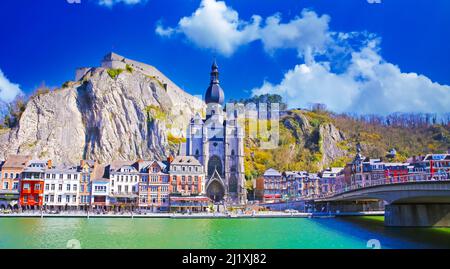 Dinant, Belgien - März 9. 2022: Blick über den Fluss maas auf eine malerische Reihe von alten bunten Häusern, Felswand mit Zitadelle, gotische Kirche gegen cle Stockfoto