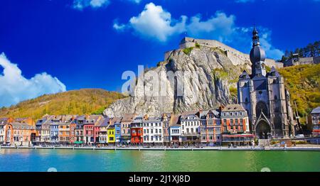 Dinant, Belgien - März 9. 2022: Blick über den Fluss maas auf eine malerische Reihe von alten bunten Häusern, Felswand mit Zitadelle, gotische Kirche gegen cle Stockfoto