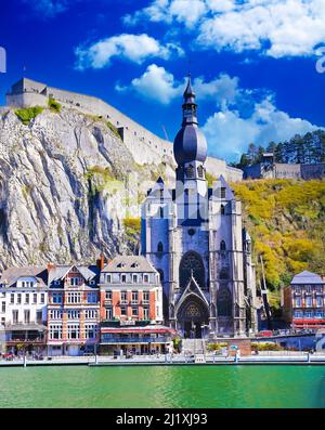 Dinant, Belgien - März 9. 2022: Blick über den Fluss maas auf eine malerische Reihe von alten bunten Häusern, Felswand mit Zitadelle, gotische Kirche gegen cle Stockfoto