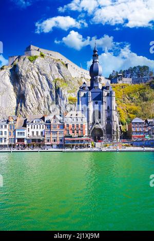 Dinant, Belgien - März 9. 2022: Blick über den Fluss maas auf eine malerische Reihe von alten bunten Häusern, Felswand mit Zitadelle, gotische Kirche gegen cle Stockfoto