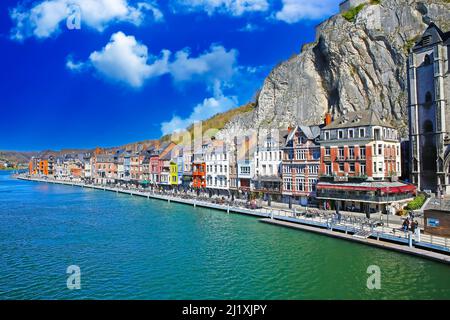 Dinant, Belgien - März 9. 2022: Blick über die gotische Kirche, Felswand auf der Uferpromenade des Flusses meuse mit Cafés und Restaurants Stockfoto